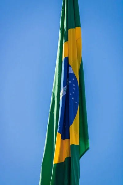 Braziliaanse vlag op paal zonder wind in de voorkant van de blauwe hemel. — Stockfoto