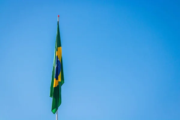 Bandeira brasileira no poste sem vento na frente do céu azul . — Fotografia de Stock