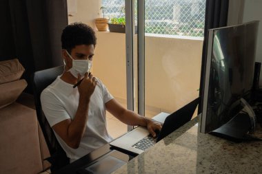 Bilgisayar masasında salgın maskesi takan siyah bir adam..