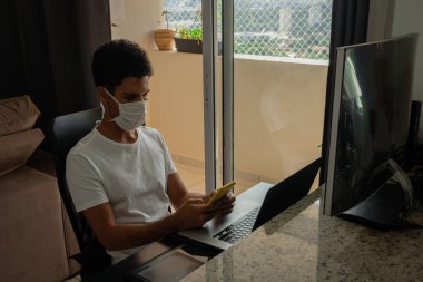 Bilgisayar masasında salgın maskesi takan siyah bir adam..