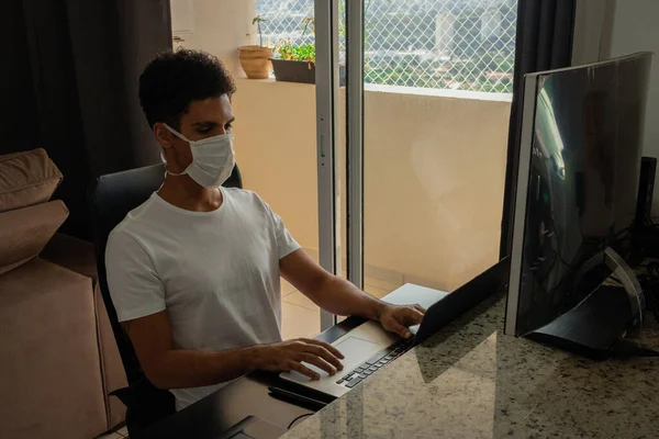 Black man at computer desk wearing pandemic mask.