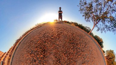Ağaçları, yumuşak mavi gökyüzü ve gün batımı olan küçük gezegende bisikleti olan bir adam. Bisiklet konsepti resmi.
