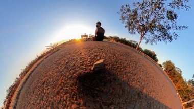 Ağaçları, yumuşak mavi gökyüzü ve gün batımı olan küçük gezegende bisikleti olan bir adam. Bisiklet konsepti resmi.
