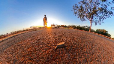 Ağaçları, yumuşak mavi gökyüzü ve gün batımı olan küçük gezegende bisikleti olan bir adam. Bisiklet konsepti resmi.