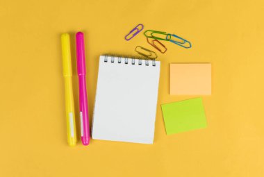 Renkli kalemler, sarı arkaplandaki çıkartmalar ve kırpıcılar gibi boş defterlerin ve okul malzemelerinin üst görünümü, metin için boşluk