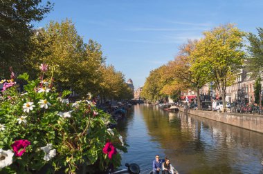 Amsterdam, Hollanda, 10 Ekim 2018: merkezi ve sakin kanallardan biri Amsterdam bulanık çiçeklerle dekorasyon Köprüsü ve çift tekne yelken