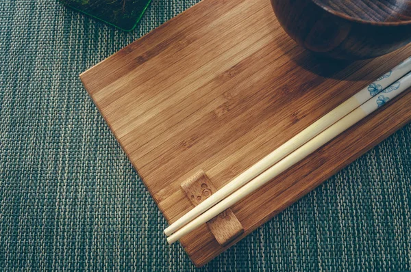 Placa de bambu com pauzinhos de madeira e tigela — Fotografia de Stock