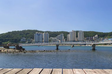 Busan, Güney Kore, 14 Eylül 2019: Songdo plajı yakınlarındaki su üstünde yürüyen köprü ve şehir manzarası üzerindeki ahşap platformdan görüntü