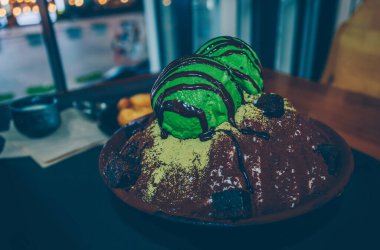 Yukarıdan çikolata, kibrit tozu ve çikolatalı kek parçalarıyla süslenmiş yeşil çay bingsu manzarası