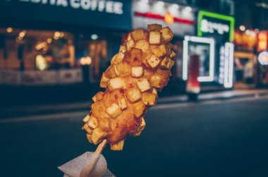 Arka planda bulanık gece manzarası olan kızarmış patatesle yapılmış Koreli mısırlı sosis.