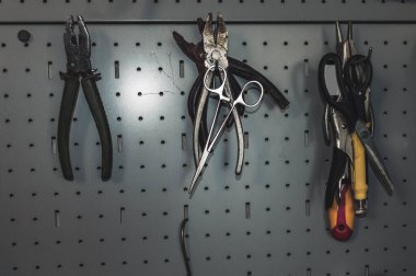 Kancalı demir tahtanın görüntüsü ve aletlere asılması: tel kesiciler, pense, makas ve tornavida.