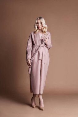 Bej renkli arka plan üzerinde pembe bir ceket poz güzel sarışın kadın. Moda giyim, mükemmel rakam, uzun saçlı olan kadın göster. Kızın cesedi trendy moda sonbahar ceket
