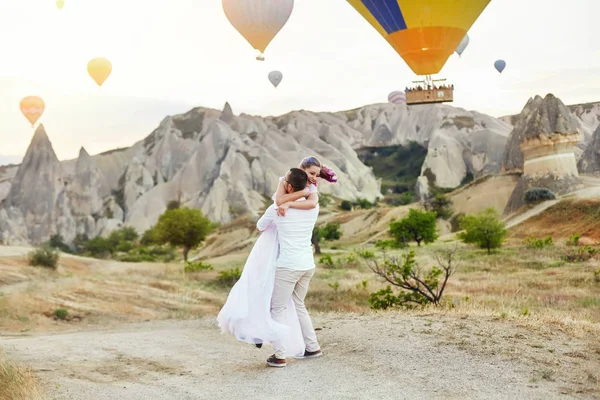 愛のカップルは カッパドキアのバルーンの背景に立っています 男と女の丘の上は 空飛ぶ風船の数が多いを見てください トルコ カッパドキア山の童話風景 自然に結婚式 — ストック写真