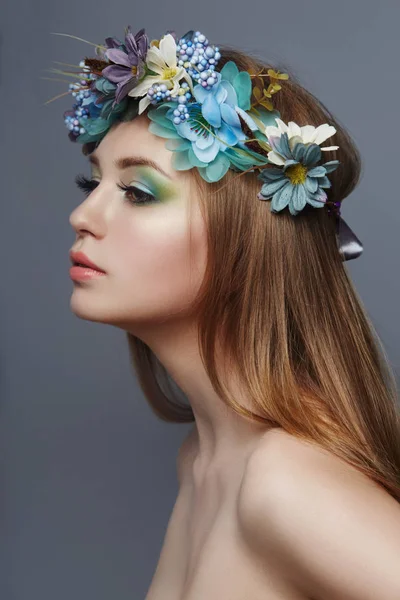 Woman with a wreath of blue flowers on her head. Beautiful makeup and flowers, natural clean skin, care and hydration. Natural cosmetics for the body, perfect lips