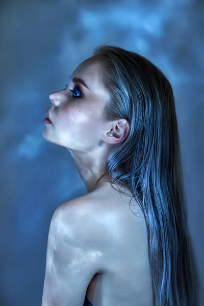 Woman with wet hair and bright makeup posing near the water, portrait. Glare from the water on the girl face, cosmetics to moisturize the skin, Spa. Woman sitting by blue pool. Art makeup on the face