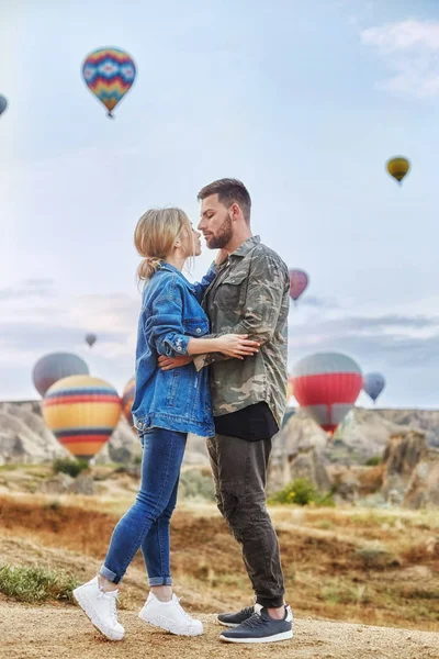 Couple in love stands on background of balloons in Cappadocia. Man and woman on hill look at a large number of flying balloons. Turkey Cappadocia fairytale scenery of mountains. Wedding on nature