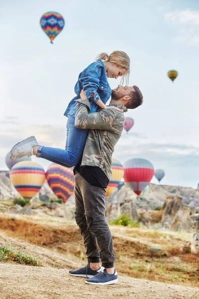 Couple in love stands on background of balloons in Cappadocia. Man and woman on hill look at a large number of flying balloons. Turkey Cappadocia fairytale scenery of mountains. Wedding on nature