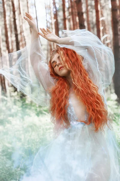 回転ダンスで森の中で青い透過光の美しい赤毛の女森のニンフのドレスします 赤い髪の女の子 夏の森のメルヘン女妖精の芸術ファッションの肖像画 — ストック写真