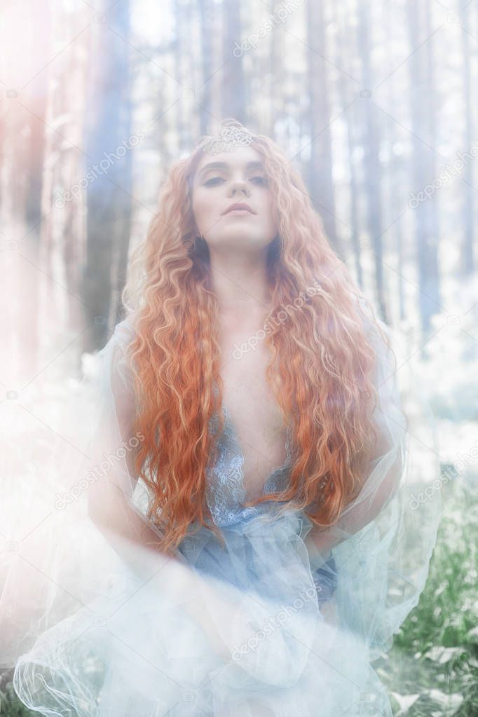 Beautiful redhead woman forest nymph in a blue transparent light dress in the woods spinning in dance. Red hair girls. Art fashion portrait of fairy woman fairy tale in summer forest