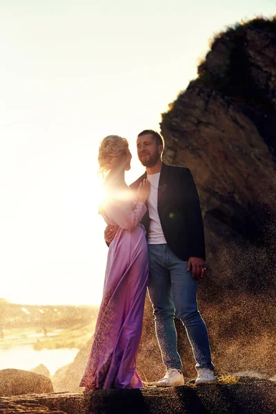 一对相爱的人站在水花对着日落的水花中 一个男人抱着一个穿着漂亮衣服的女人 爱在眼睛里 — 图库照片
