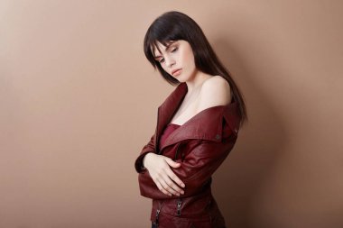 Sexy brunette in leather jacket and red top, portrait bright makeup and lipstick close-up, face makeup, professional makeup, skin care. Young sexy woman posing on beige background, flying hair