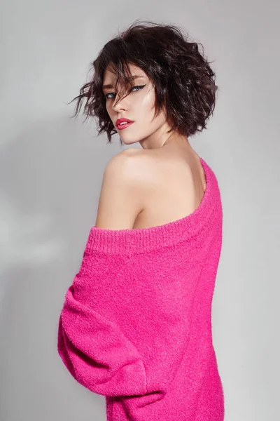 Sexy woman with short hair cut in pink red sweater on white background. Perfect girl with wet tousled dark hair and bright makeup, short hair, beauty and hair care. Naked shoulder women