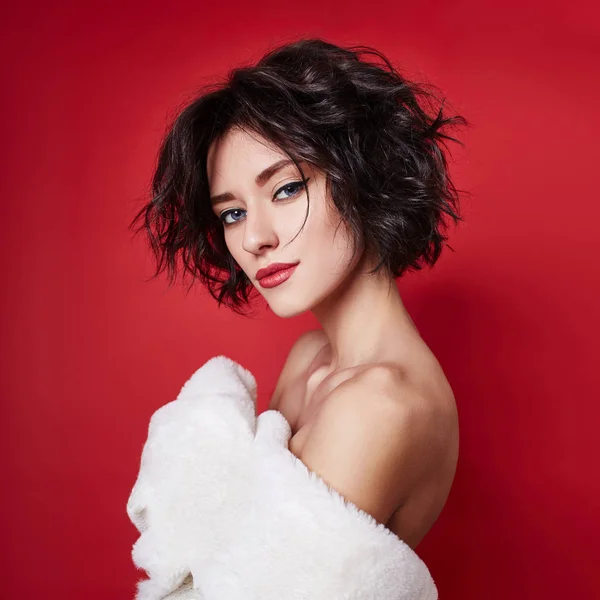 Sexy woman with short hair cut in white sweater on red background. Perfect girl with wet tousled dark hair and bright makeup, short hair, beauty and hair care. Naked shoulder women