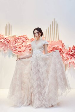 Lüks kadın güzel bir pahalı gelinlik büyük yapay çiçek arka plan üzerine gelin. Beyaz tatil elbiseli kız mükemmel saç ve makyaj. Dantel elbise genç bir kadının vücudunda