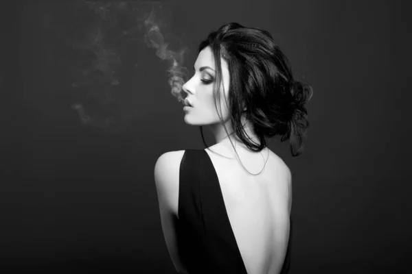 Art Brunette kouří na tmavém pozadí v černých šatech. Cl — Stock fotografie