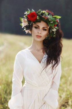 Uzun elbiseli bir kız kafasında çelenkle bir tarlada duruyor.