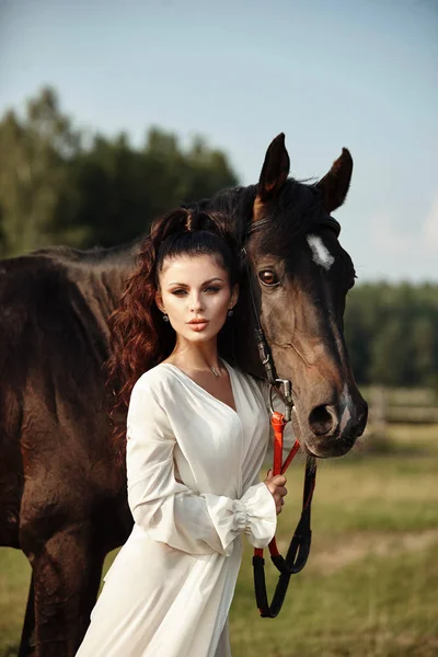 Meisje in een lange jurk staat naast een paard, een mooie vrouw stro — Stockfoto