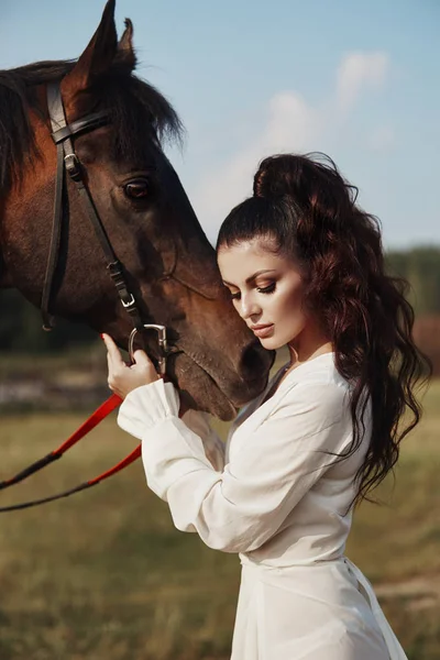 Meisje in een lange jurk staat naast een paard, een mooie vrouw stro — Stockfoto