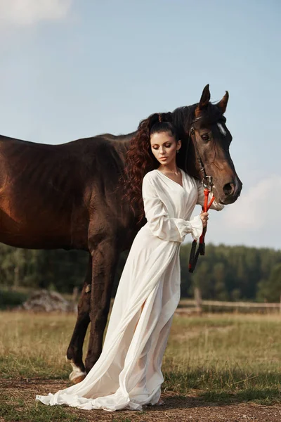 Meisje in een lange jurk staat naast een paard, een mooie vrouw stro — Stockfoto