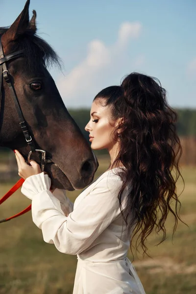 Meisje in een lange jurk staat naast een paard, een mooie vrouw stro — Stockfoto