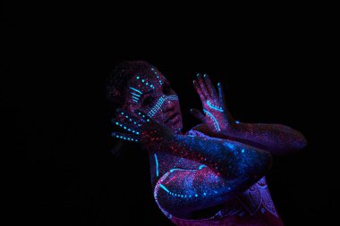 Kadın yoga yapıyor, el hareketi yapıyor, vücut ısıtması yapıyor. Sanat kızı ultraviyole ışıkta kozmos oynuyor. Bütün vücudu renkli damlacıklarla kaplı. Astral yoga. Gürültü, odak dışı