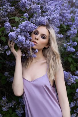 Yazın leylak çalılığında sarışın güzel bir kadın. Mor çiçekli bir kızın güzel portresi, güzel bir makyaj.