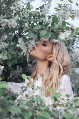 Yazın Elma ağacının dallarında seksi sarışın kadın. Beyaz Elma çiçekleri içindeki bir kızın portresi