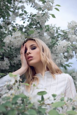 Elma bahçesindeki beyaz elbiseli bir kadının portresi. Elma çiçekli bir kızın yüzü kapanıyor.