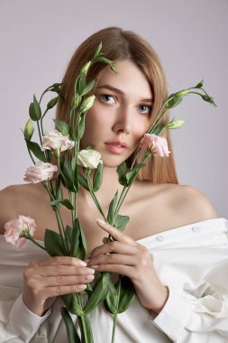 Elinde pembe Eustoma çiçekleri olan güzel bir portre kadın. Yüz ve vücut bakımı için doğal kozmetik ürünleri. Beyaz gömlekli güzel kız.