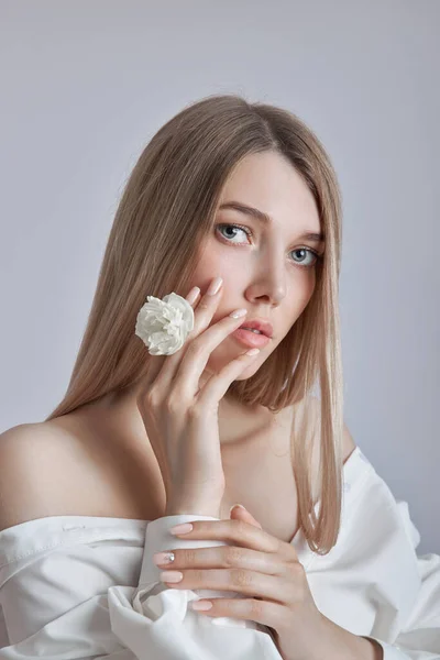 Blonde beauty woman holds white flower in hand. Beautiful soft hands and soft skin. Cosmetics for beauty hand care