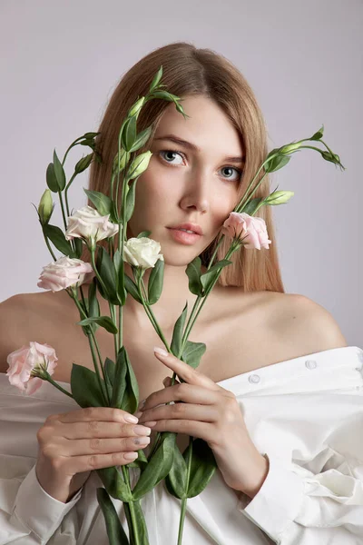 Elinde pembe Eustoma çiçekleri olan güzel bir portre kadın. Yüz ve vücut bakımı için doğal kozmetik ürünleri. Beyaz gömlekli güzel kız.