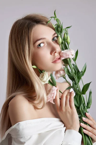 Elinde pembe Eustoma çiçekleri olan güzel bir portre kadın. Yüz ve vücut bakımı için doğal kozmetik ürünleri. Beyaz gömlekli güzel kız.