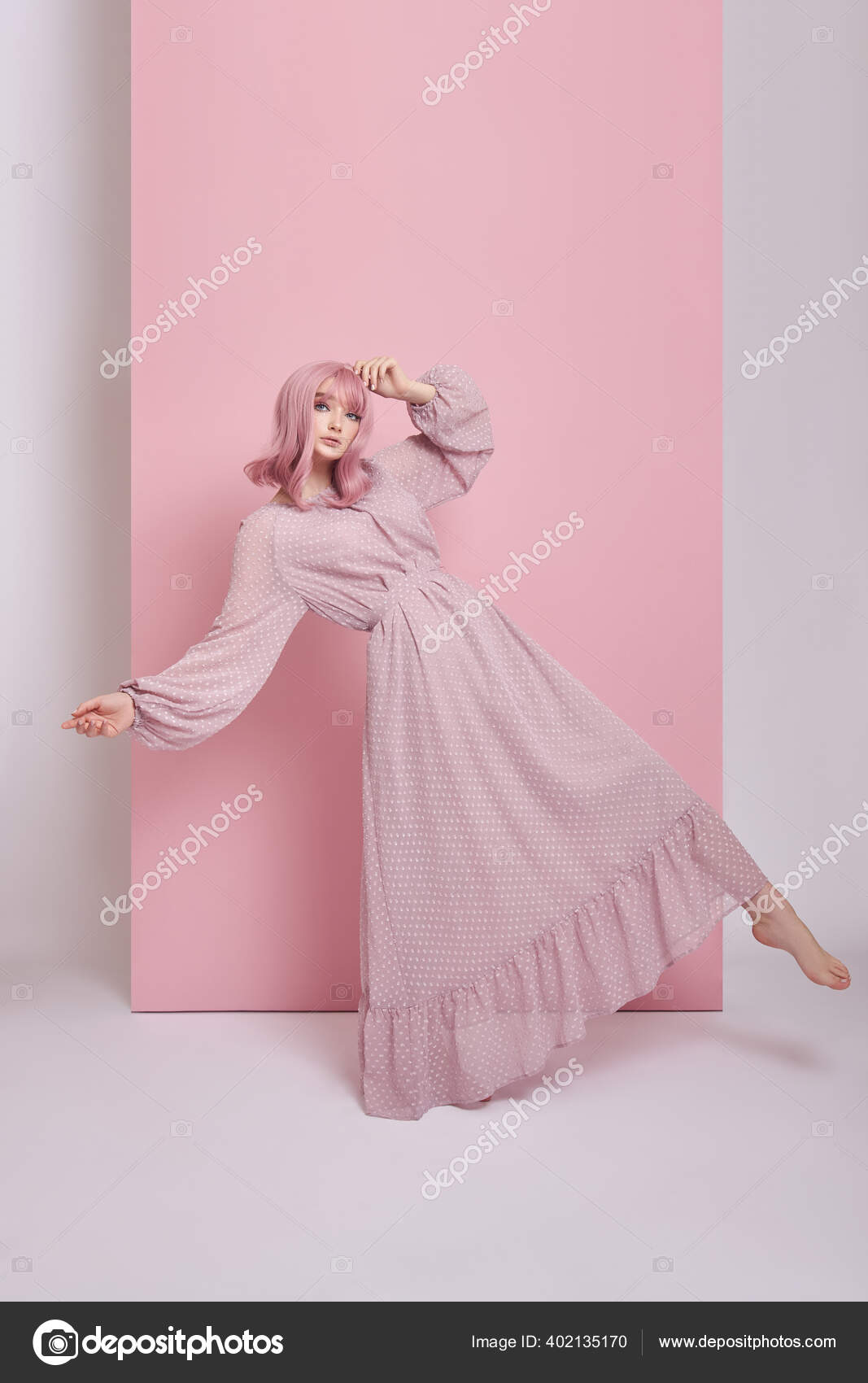 Uma mulher com um vestido rosa fica em frente a uma parede de