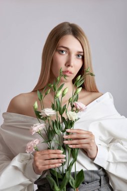 Elinde pembe Eustoma çiçekleri olan güzel bir portre kadın. Yüz ve vücut bakımı için doğal kozmetik ürünleri. Beyaz gömlekli güzel kız.