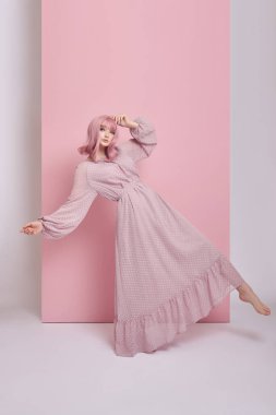 Uzun elbiseli, boyalı pembe saçlı bir kadın. Pembe duvarda saç boyası olan bir kızın portresi. Mükemmel saç stili ve saç şekli