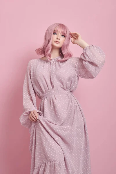 Woman with dyed pink hair in a long dress. Portrait of a girl with hair coloring at the pink wall. Perfect hairstyle and hair styling
