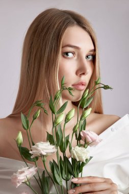 Elinde pembe Eustoma çiçekleri olan güzel bir portre kadın. Yüz ve vücut bakımı için doğal kozmetik ürünleri. Beyaz gömlekli güzel kız.