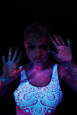 Kadın yoga yapıyor, el hareketi yapıyor, vücut ısıtması yapıyor. Sanat kızı ultraviyole ışıkta kozmos oynuyor. Bütün vücudu renkli damlacıklarla kaplı. Astral yoga. Gürültü, odak dışı