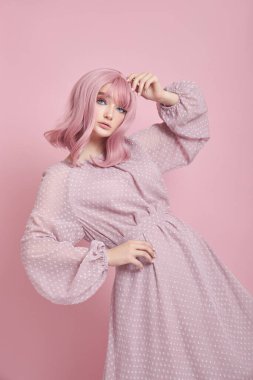 Uzun elbiseli, boyalı pembe saçlı bir kadın. Pembe duvarda saç boyası olan bir kızın portresi. Mükemmel saç stili ve saç şekli