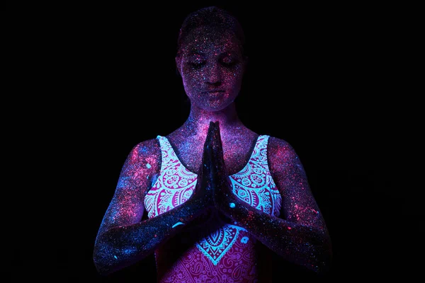 Woman does yoga, hand movement, body warm-up. Art girl cosmos in ultraviolet light. Entire body is covered with colored droplets. Astral yoga. Noise, out of focus